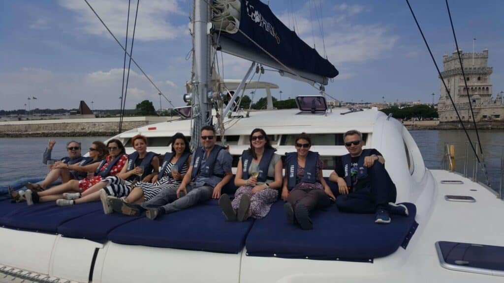 Pessoas sentadas na proa do catamaran com a Torre de Belém ao fundo