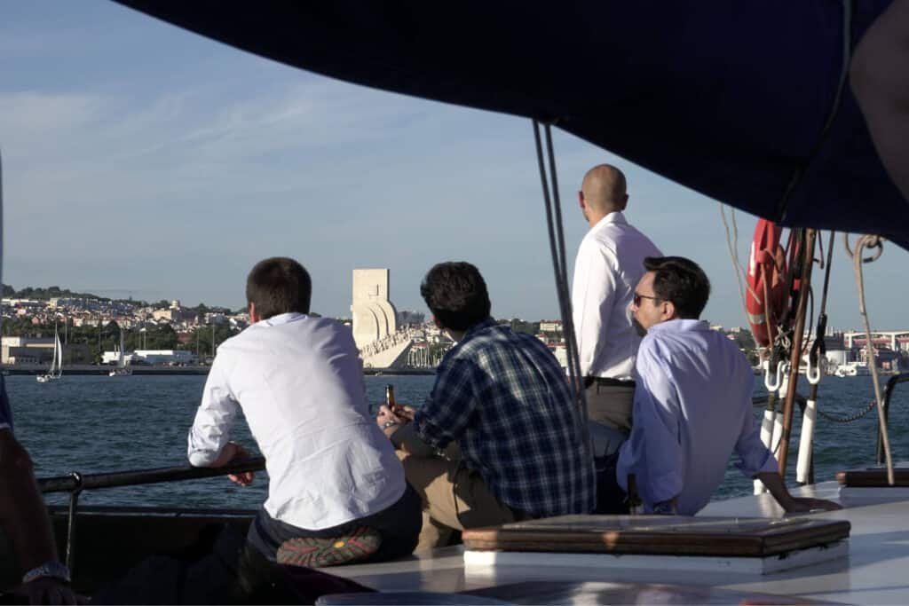 Homens descontraídos num barco a observar o Padrão dos Descobrimentos