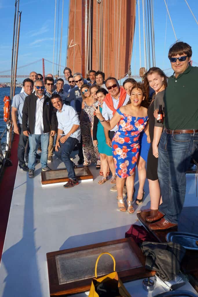 Grupo de pessoas num veleiro clássico com a ponte sobre o Tejo ao fundo