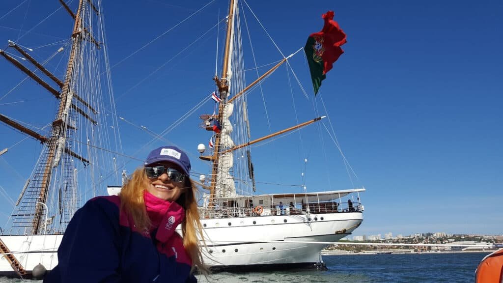 Rapariga num barco, com o navio Sagres como pano de fundo, durante a regata Volvo Ocean Race