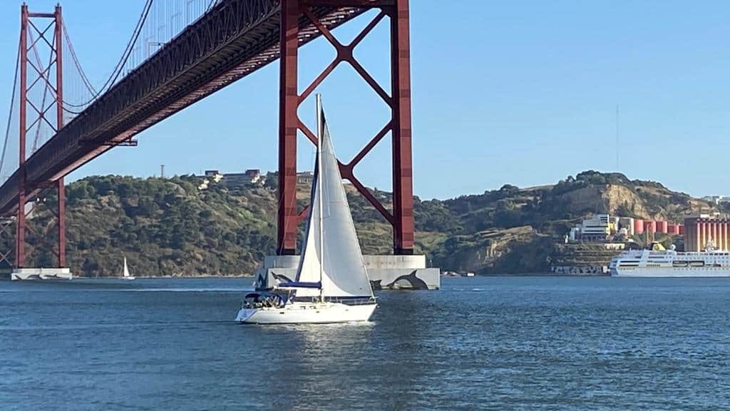 Veleiro a navegar por baixo da ponte sobre o rio Tejo